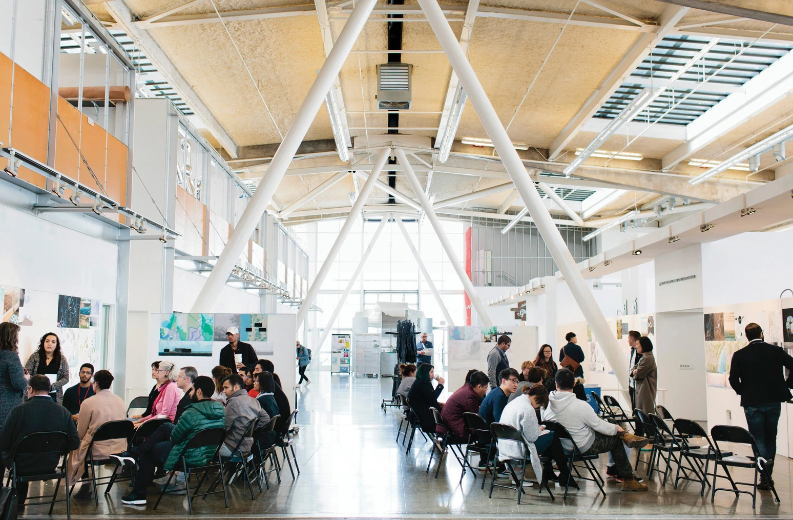 Two groups of CCA students sit in black folding chairs on opposite sides of the nave of the main SF campus building
